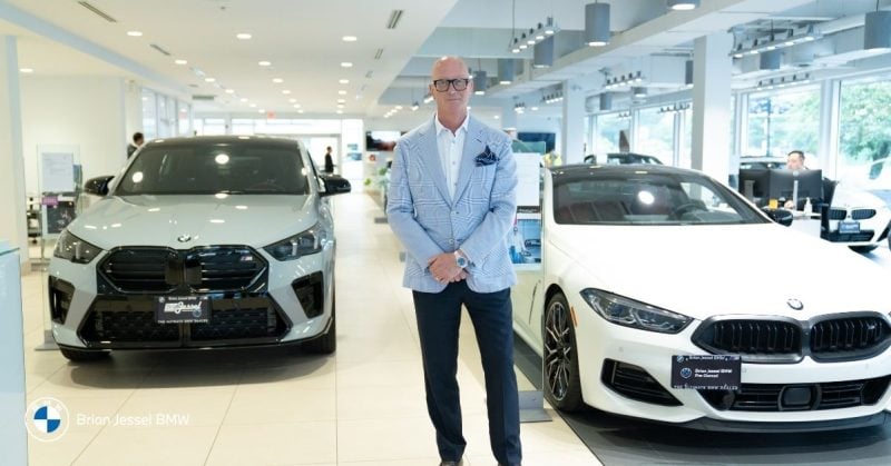 A person stands in the Brian Jessel BMW dealership showroom with two BMW cars on display.