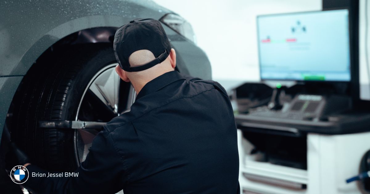 Mechanic adjusting a car wheel using diagnostic equipment inside an auto service bay with computer screen