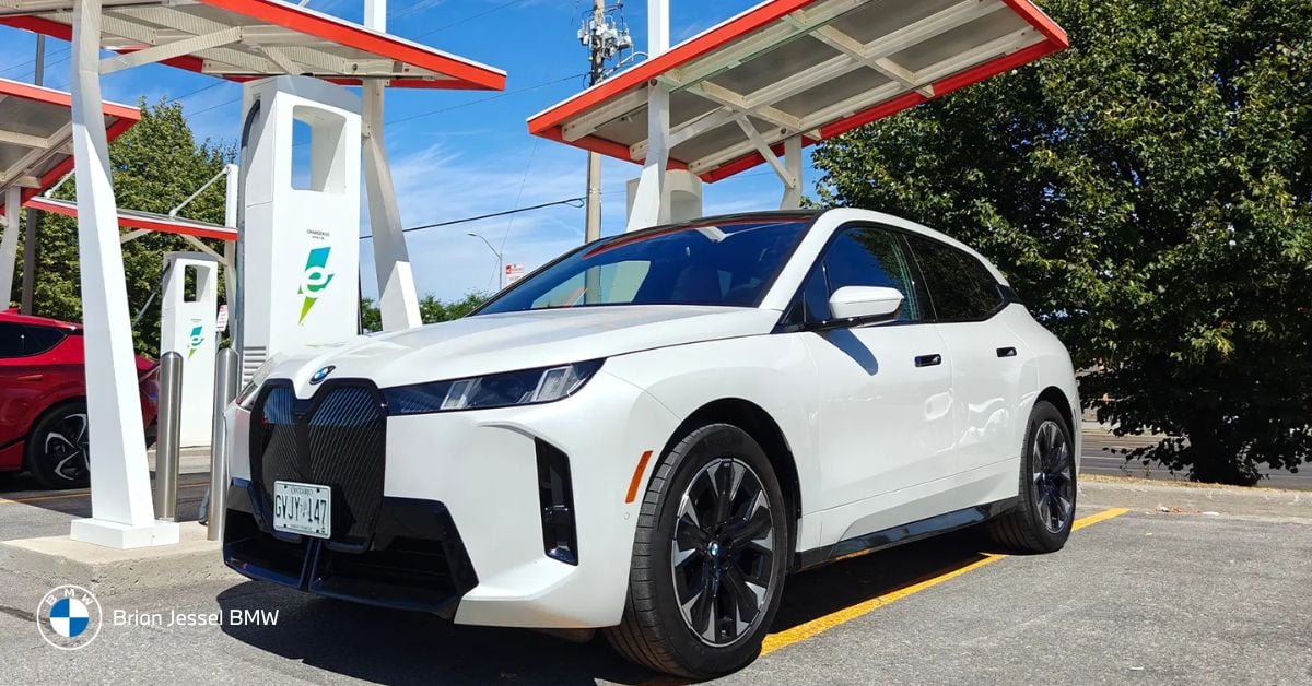 White BMW iX charging at an EV station under solar canopies on a bright, sunny day.