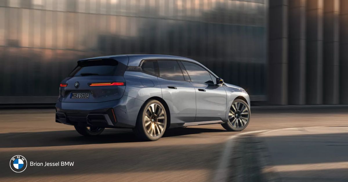 Rear three-quarter view of a moving BMW iX in sunlight, highlighting sleek design and wheels.