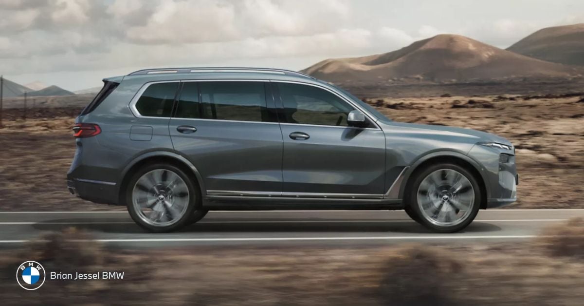 Side view of a gray BMW SUV driving on a desert highway with mountains in the background