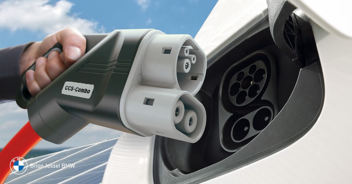 Person plugging a CCS Combo electric vehicle charger into a BMW iX charging port unit.