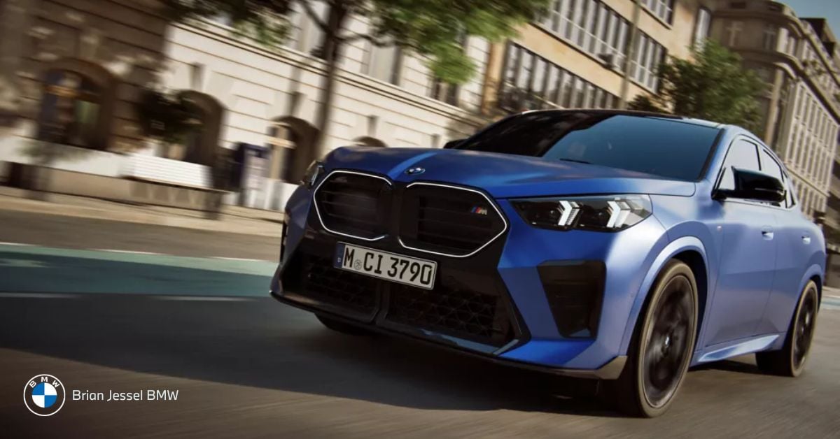 Blue BMW X2 drives through city streets, showcasing sporty compact design, aggressive stance, and urban performance appeal.