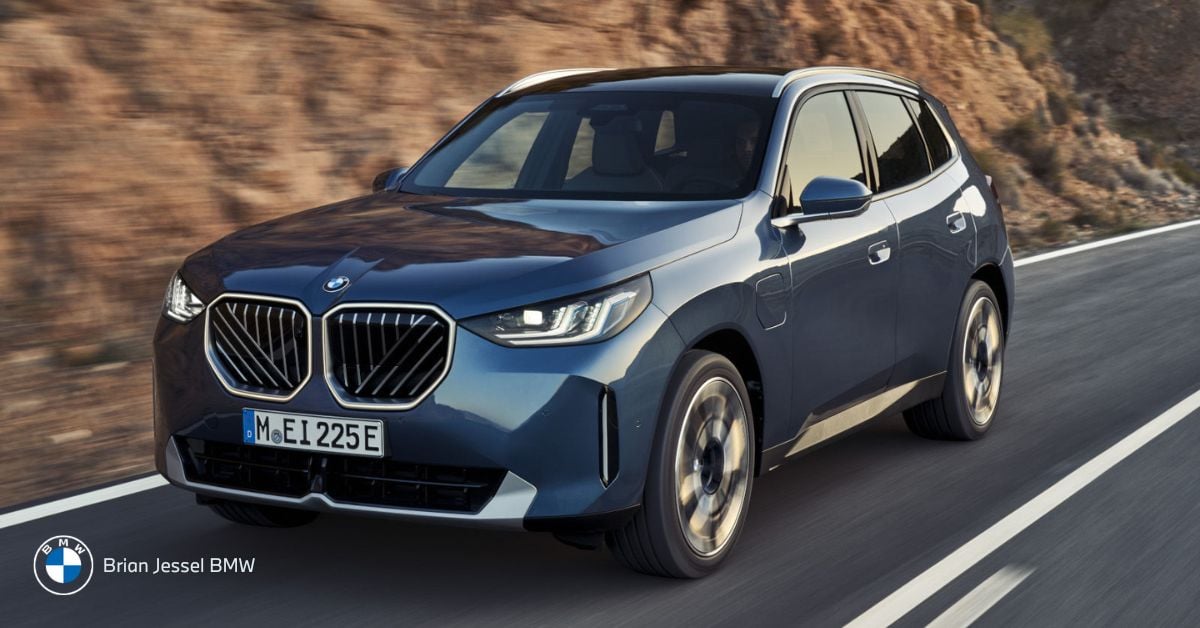 A blue BMW X3 driving on a highway beside rocky terrain, showing its sporty SUV design.