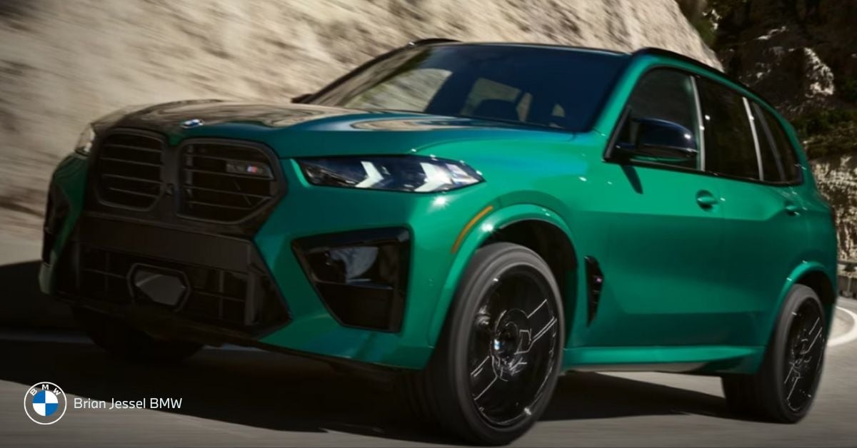 Green BMW X5 M Competition SUV drives dynamically on mountain road, showcasing aggressive design and performance stance