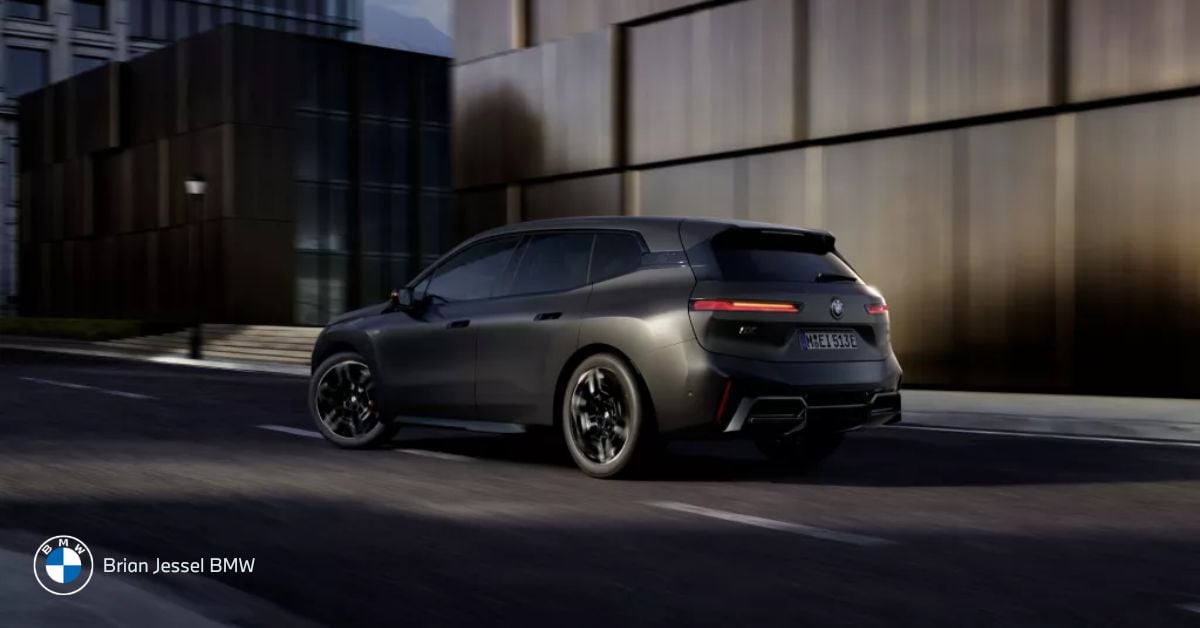 Matte gray BMW iX M70 SUV accelerates through city street, showcasing sleek electric performance design