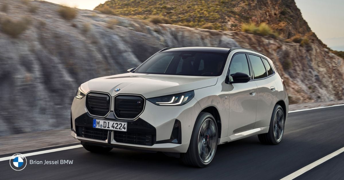 A white BMW SUV driving on a mountain highway with rocky hills behind and clear skies.