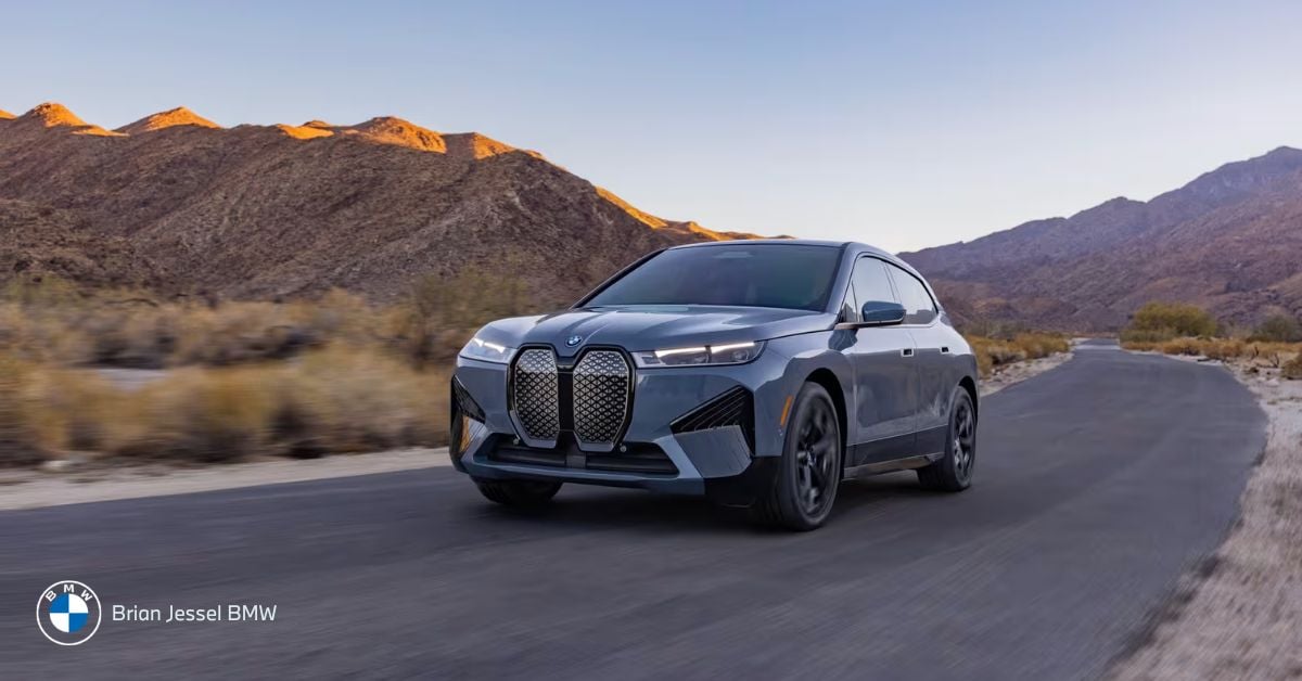 A sleek BMW iX electric SUV driving along a winding mountain road during a vibrant sunset.