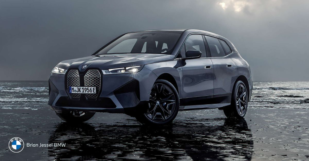 A sleek BMW iX electric SUV parked on a dark, wet surface under a cloudy sky.