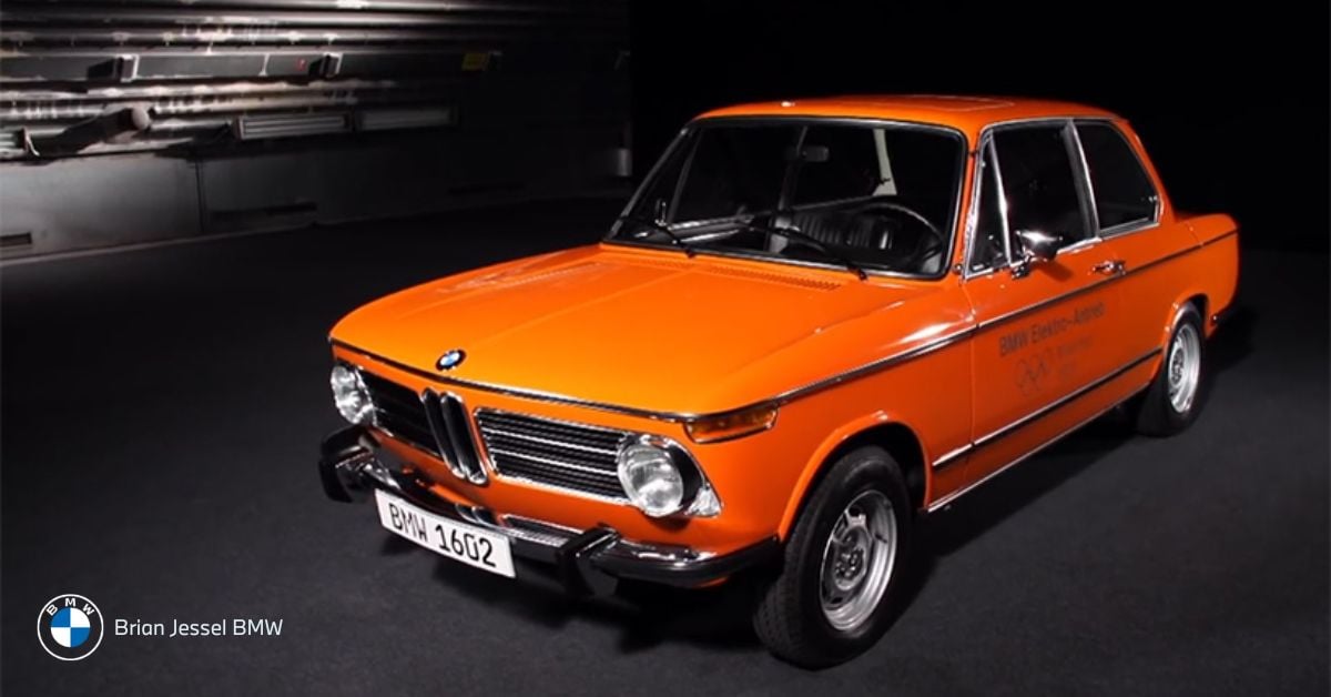 An orange vintage BMW 1602 Elektro-Antrieb sits under studio lights, showcasing early electric car innovation