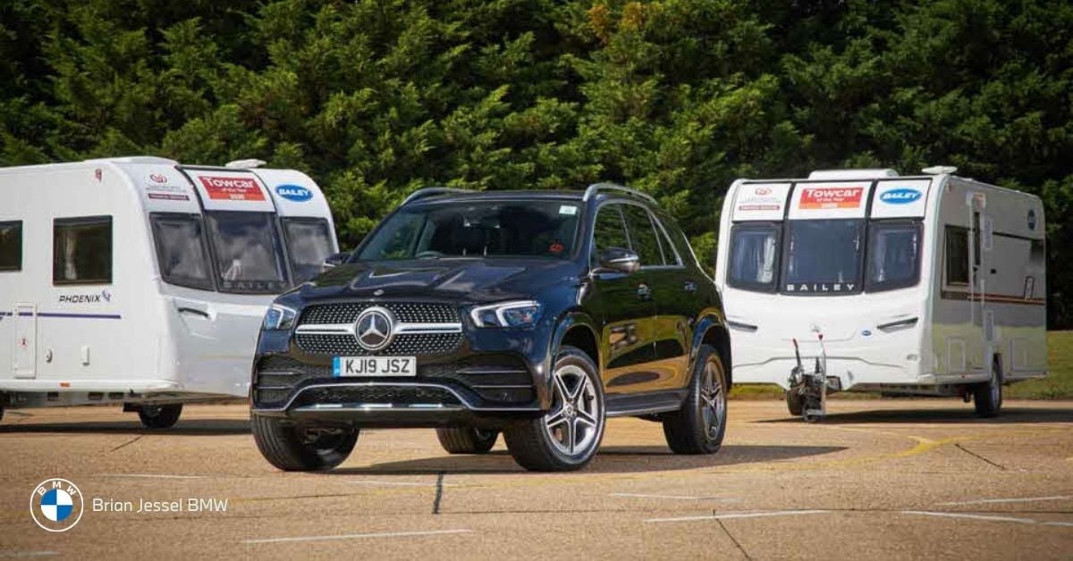 Black Mercedes-Benz GLE SUV parked between two white caravan trailers on a sunny paved lot