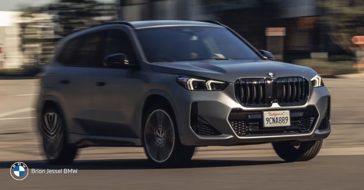 BMW X1 xDrive driving on city street, front-side view, compact all-wheel-drive SUV, winter-ready, urban-capable vehicle.