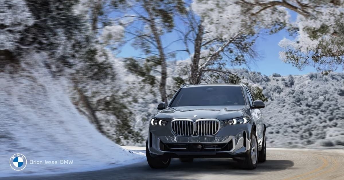 BMW X5 xDrive SUV driving dynamically on a snowy, tree-lined mountain road in bright winter sunlight