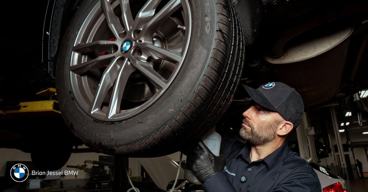 Mechanic inspecting BMW winter tire on lifted vehicle, close-up view, focusing on wheel, tire tread, safety maintenance.