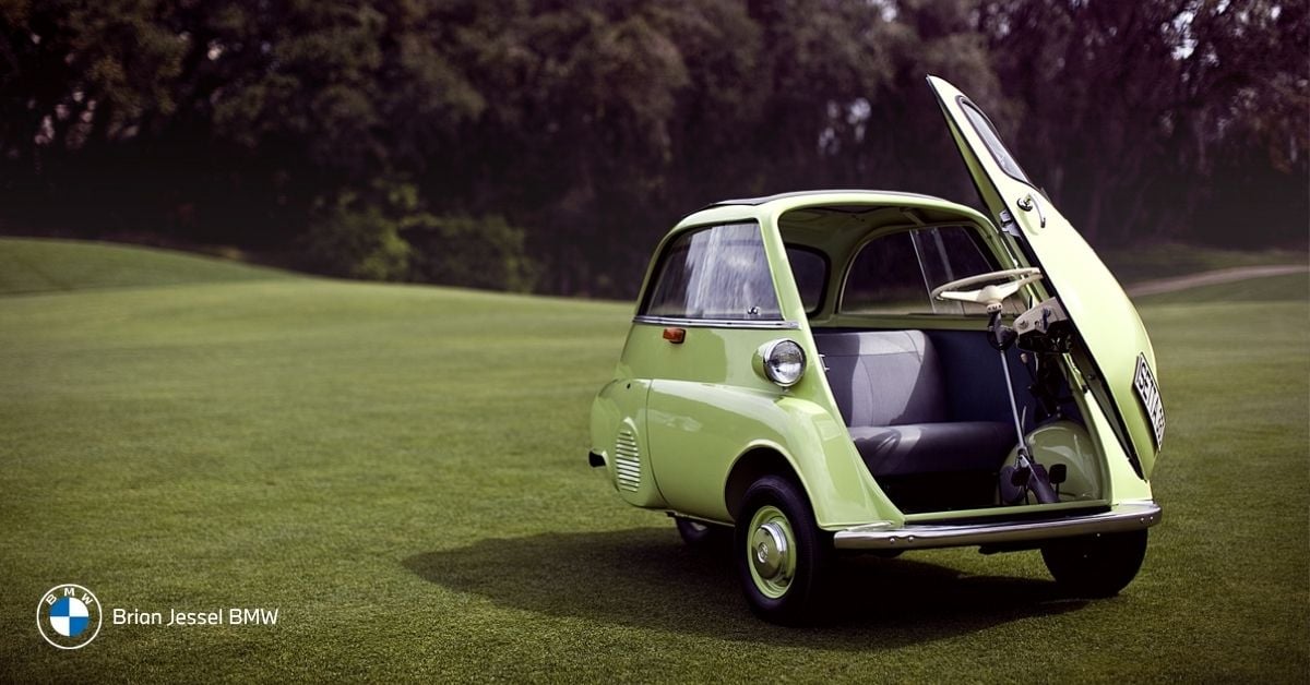 Light green BMW Isetta with its iconic front door fully open, parked on a lush green lawn.