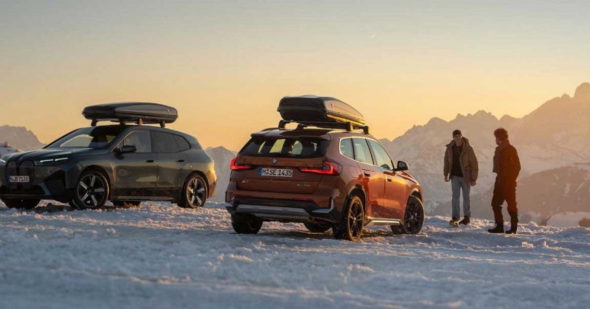 Two BMW SUVs with roof boxes parked in snow with mountain backdrop at sunset, ideal for Whistler winter trips