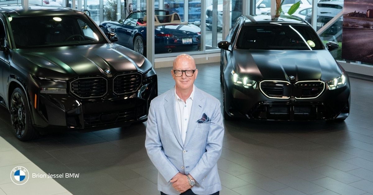 Brian BMW manager standing between two black BMW SUVs inside the Brian Jessel BMW showroom