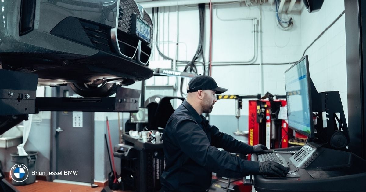 BMW technician working on vehicle in service bay using diagnostic computer, representing maintenance and service costs in Vancouver