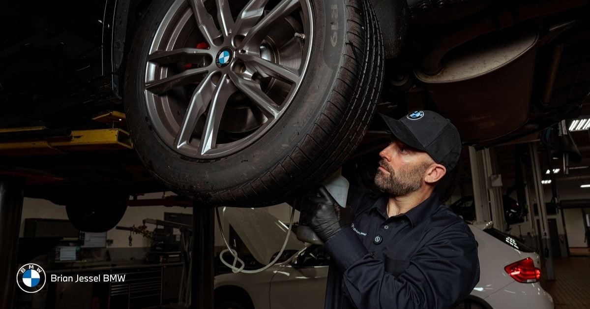 BMW technician inspecting tire condition and wheel components during BMW tire service and maintenance appointment at dealership service centre.