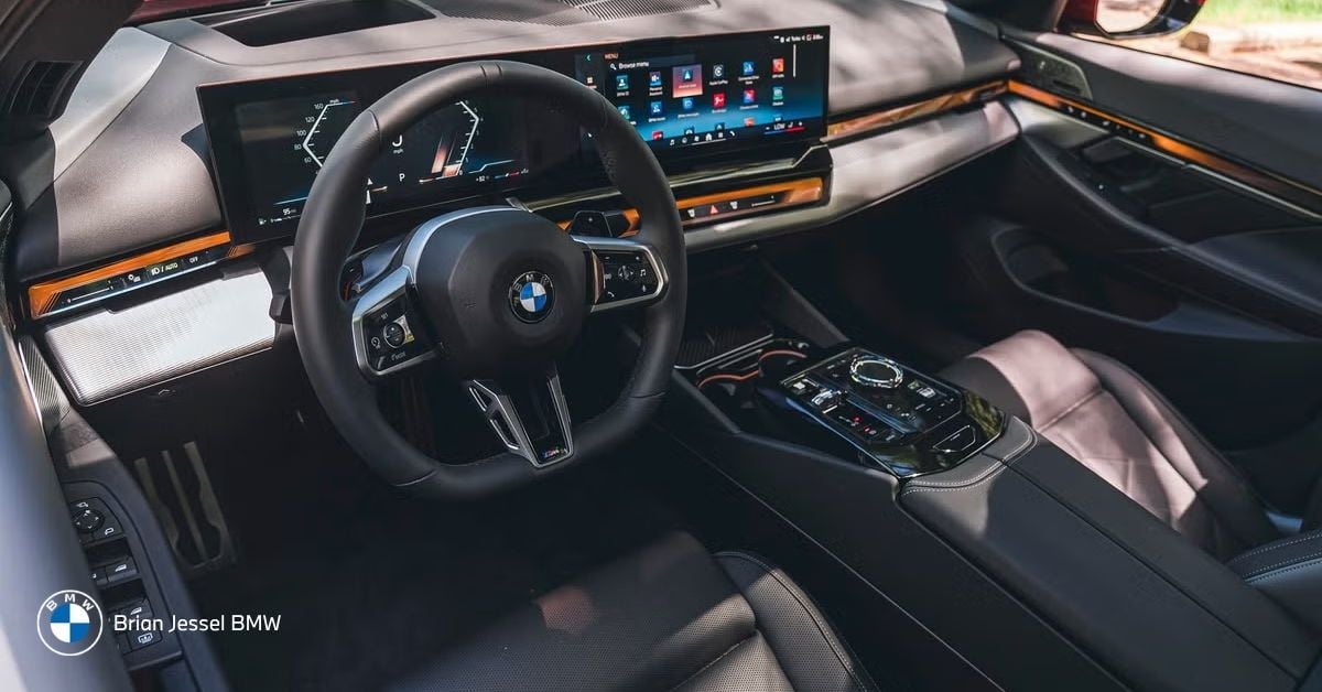 Premium BMW 5 Series interior with expansive curved digital displays, luxurious leather seats, and sophisticated wood trim accents.