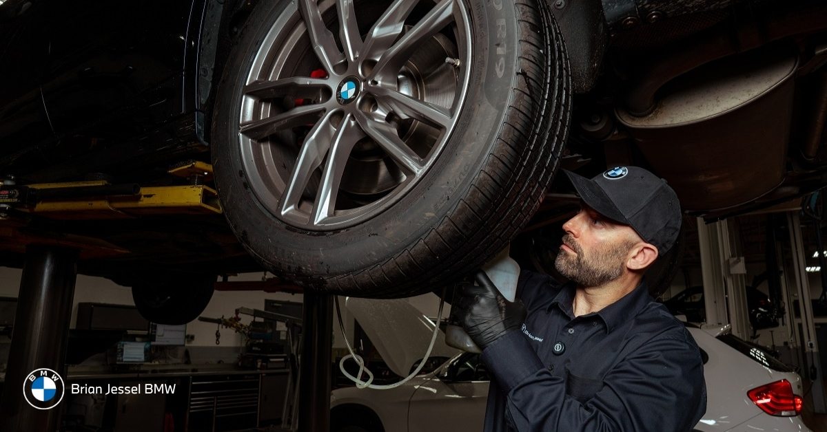 BMW technician carefully inspecting tire on elevated vehicle in Brian Jessel BMW professional service bay.