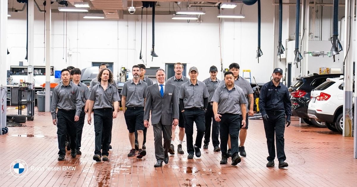 Group of certified BMW technicians led by a manager in suit walking forward in the bright professional service workshop at Brian Jessel BMW in Vancouver Canada.