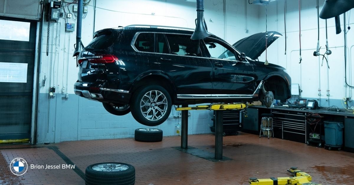 Black BMW SUV elevated on yellow hydraulic lift in modern service bay, hood open and wheels removed.