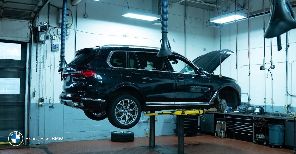 BMW SUV undergoing service inspection on hydraulic lift inside authorized dealership workshop with professional maintenance equipment.