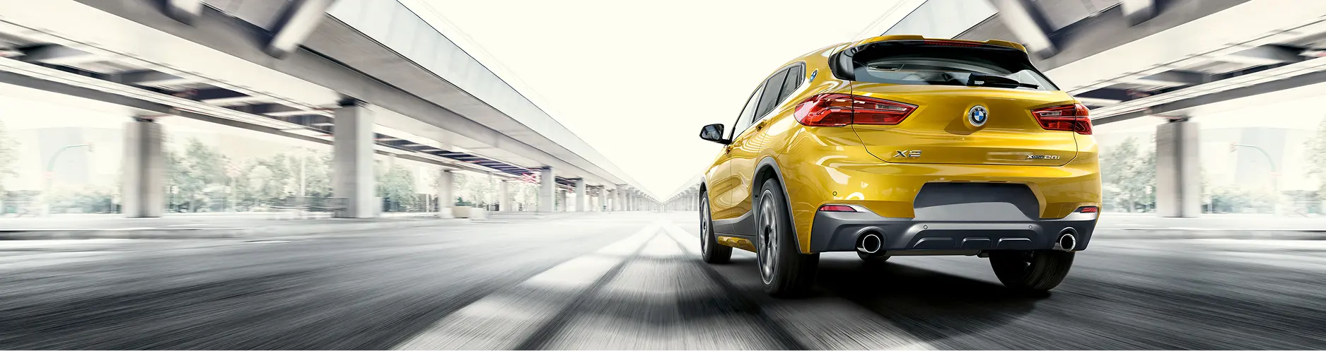 Yellow BMW X2 on a highway under a bridge