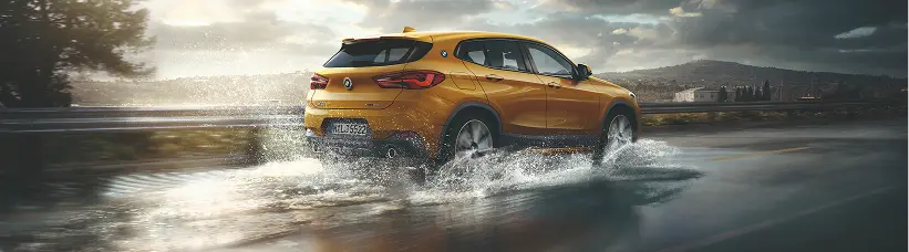 Yellow BMW X2 driving through water at sunset