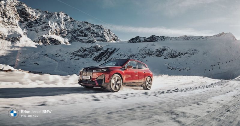 Electric BMW iX in action on snow-covered terrain with snowy peaks in the distance