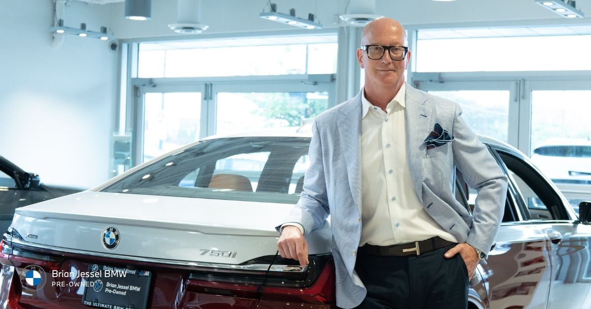 standing next to a BMW 750i, showcasing luxury vehicle shopping