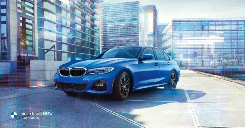 Blue BMW 3 Series parked in front of modern glass buildings, showcasing sleek design