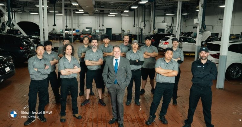 Group of professionals at Brian Jessel BMW, standing proudly in a service garage with BMWs.