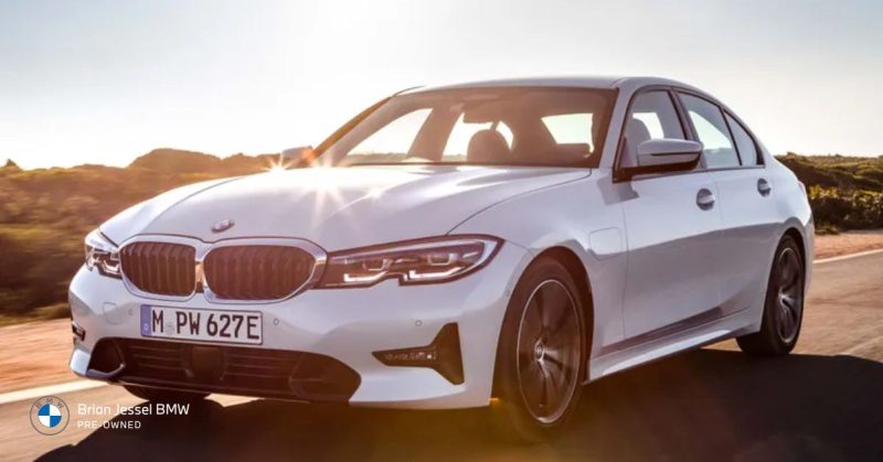 BMW 3 Series in white driving on a scenic road with sunlight reflecting on the car