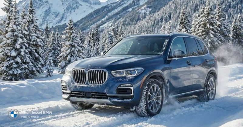 Blue BMW SUV driving through snowy forest, representing winterized vehicle performance, proper fluids, brakes, and cold-weather maintenance readiness for safety.