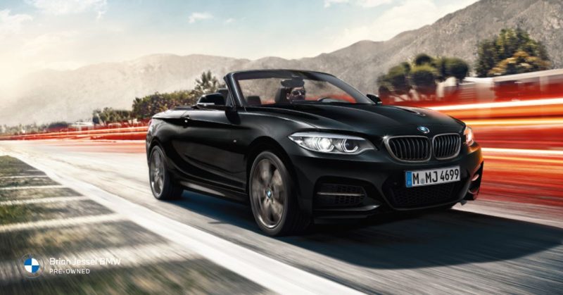 BMW 2 Series black convertible speeding on a scenic road, blending luxury with performance
