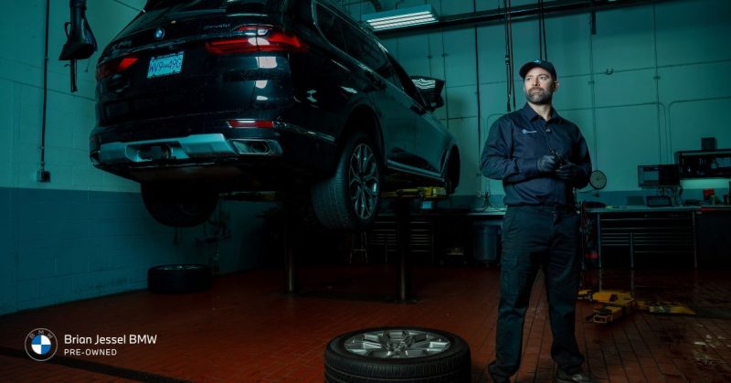 BMW technician standing in a service bay next to an elevated vehicle, ready for maintenance.