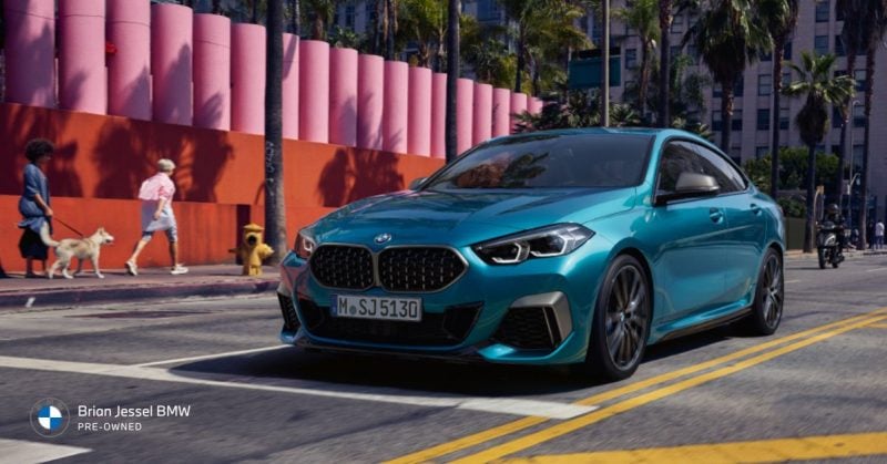  Sporty BMW 2 Series coupe in teal driving through a dynamic urban environment with pedestrians