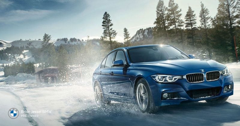 Blue BMW sedan driving through snowy mountain road, illustrating winter driving conditions, traction challenges, and importance of proper vehicle maintenance. 