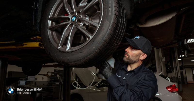 BMW technician inspecting tire and wheel, ensuring vehicle performance and maintenance at a service center
