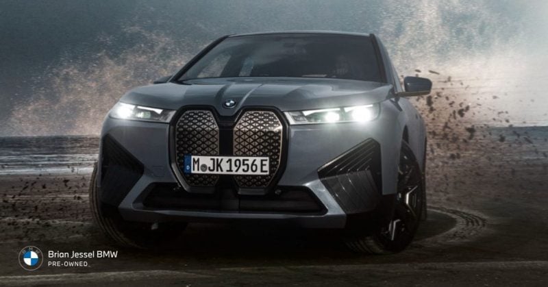 2023 BMW iX M60 electric SUV driving through wet terrain, showcasing all-wheel drive traction, bold design, and performance