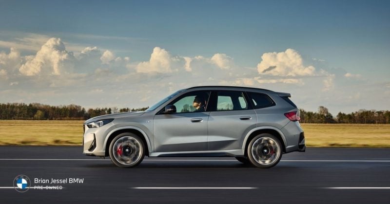 Silver BMW X1 driving on a scenic road with motion blur, showcasing its sporty design and urban agility