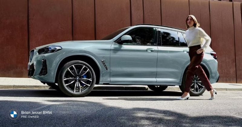 Light blue BMW X3 parked on a city street with a woman walking beside it, highlighting its stylish design
