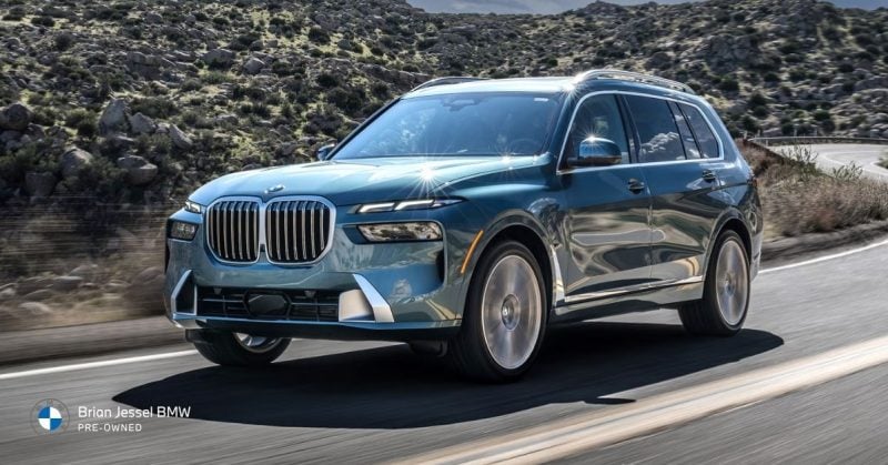 Blue BMW X7 driving dynamically on a winding mountain road, showcasing its commanding presence and spacious design