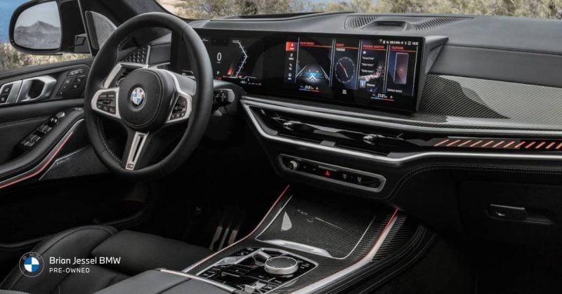 Modern black BMW SUV interior with large digital dashboard, curved display, leather steering wheel, and premium carbon fiber trim