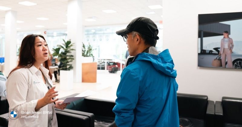  A woman in a white shirt explains certified pre-owned benefits to a customer in a BMW dealership showroom