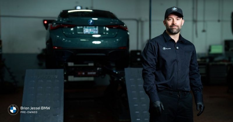 BMW technician in uniform standing in service bay beside a green BMW elevated on a lift at Brian Jessel BMW.