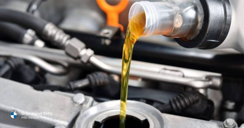 Golden engine oil being poured from a bottle into the open oil filler cap of a BMW engine during service.