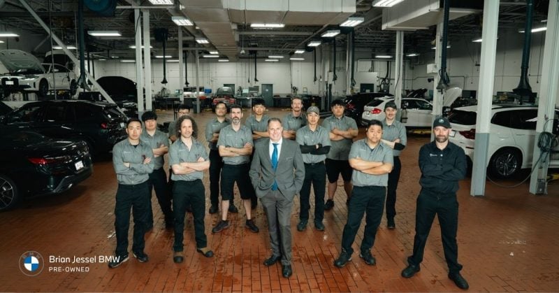 Team of Brian Jessel BMW Pre-Owned technicians and manager posing together in the Vancouver service center with BMW vehicles